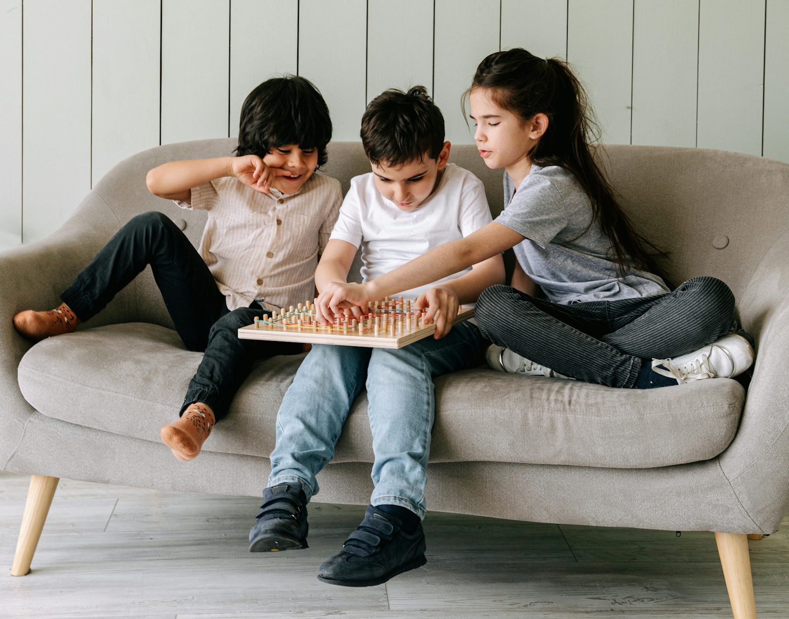 Three children sitting on a couch playing a board game together Чем занять ребёнка дома, чтобы он забыл про гаджеты: практичные советы родителей и психологов