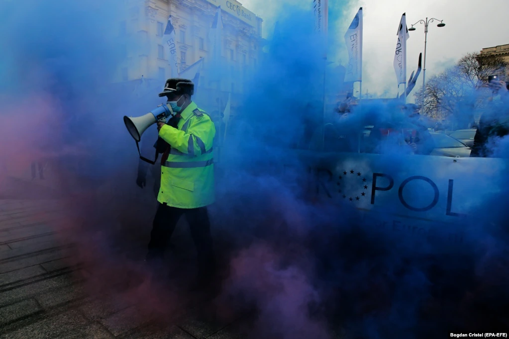 Офицер полиции идет сквозь цветной дым во время акции протеста с требованием повышения заработной платы и условий для полицейских перед зданием Министерства внутренних дел Румынии 25 марта